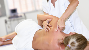 Fisioterapeuta profesional dando masaje en el hombro a una mujer rubia en un hospital. Revisión médica en el hombro en un centro de fisioterapia.